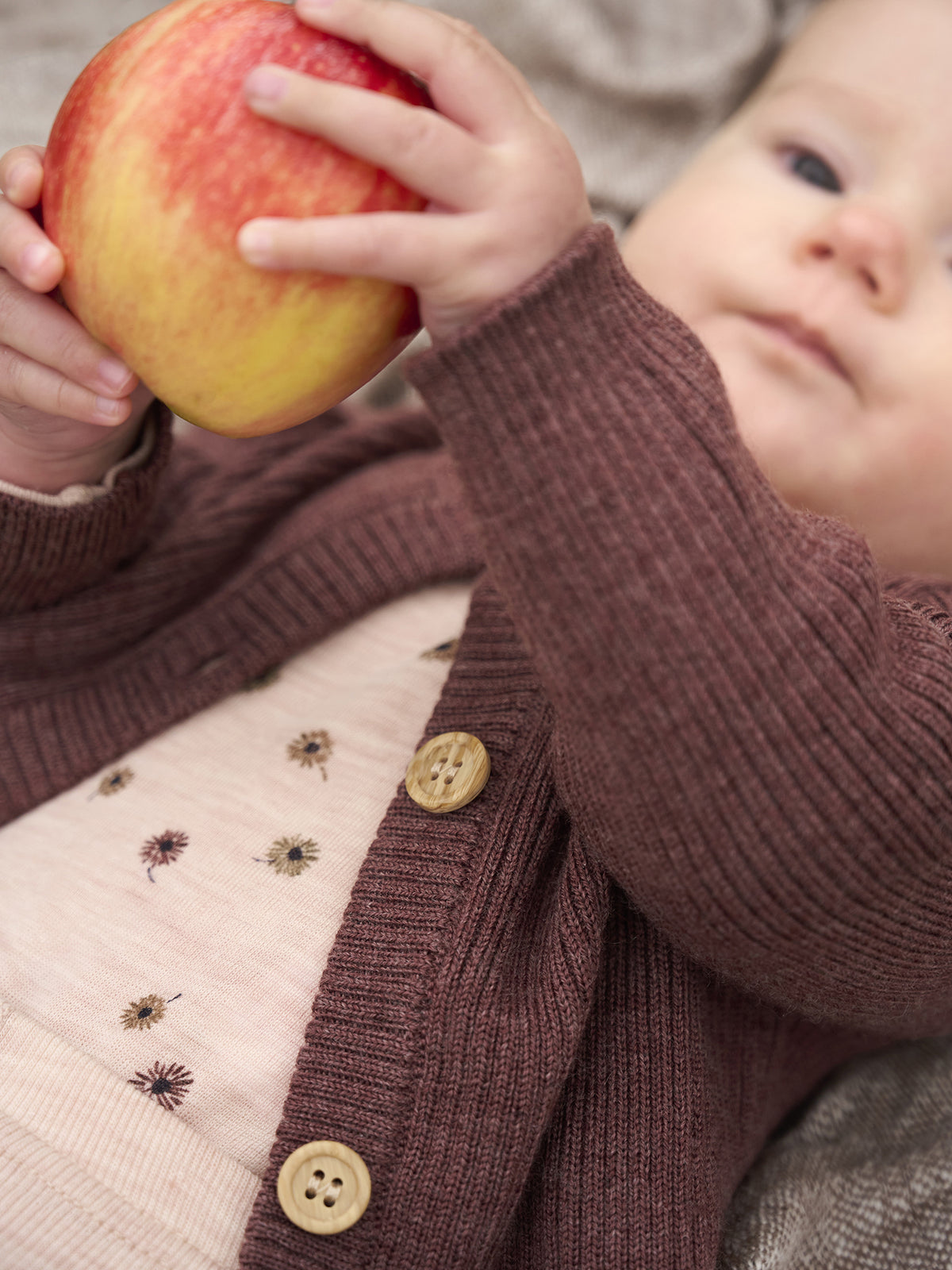 Kleinkind trägt CeLaVi Cardigan in Marron und hält Apfel – erhältlich im Bärechind in Winterthur, Zürich, Schweiz.