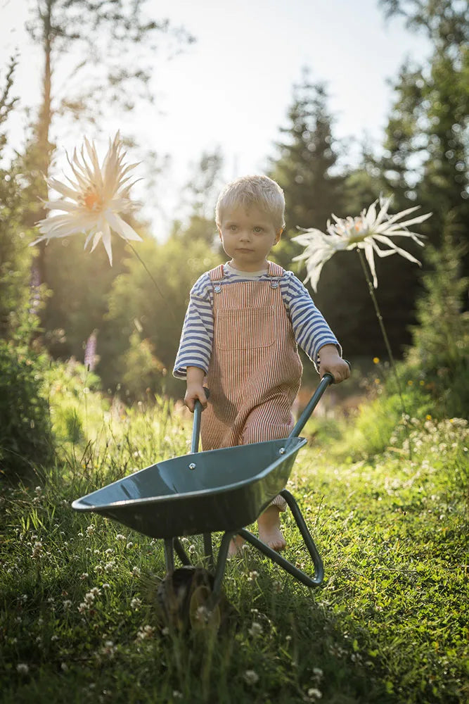 Kind spielt mit grüner Kinder Schubkarre aus Metall im Garten – erhältlich bei Bärechind Winterthur Zürich Schweiz.