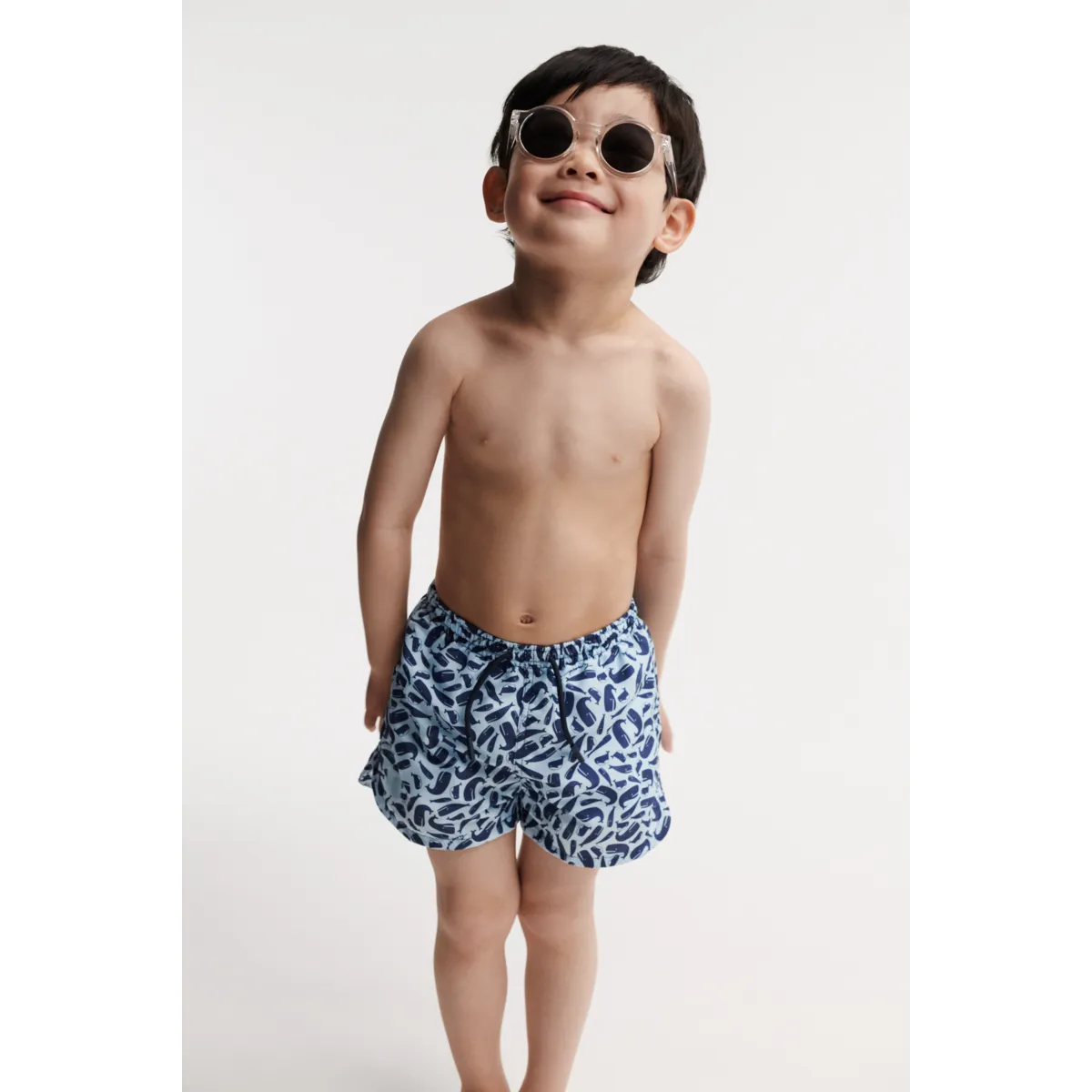 Kind trägt die Liewood Aiden Board Shorts in Ocean Pure Sky am Strand. UV-Schutz UPF 40+, schnell trocknend und bequem. Erhältlich in Winterthur, Zürich, Schweiz.