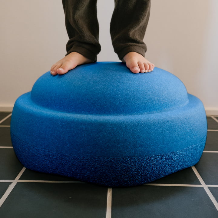 Kind steht auf einem grossen blauen Schaumstoff-Balanceelement auf dunklen Bodenfliesen.