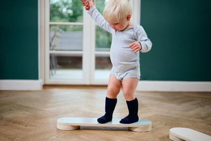 Baby mit navyefarbenen GoBabyGo Wollsocken auf Holzfussboden – sicherer Halt beim Laufenlernen