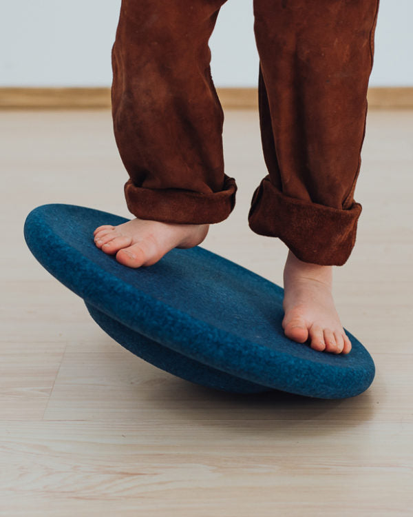Kind balanciert barfuss auf dem dunkelblauen Balance Board – Bewegungsspielzeug bei Bärechind in Winterthur, Schweiz