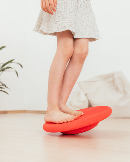 Chind balanciert barfuss auf rotem Stapelstein Balance Board – Spiel und Bewegung im Bärechind, Winti, Schweiz