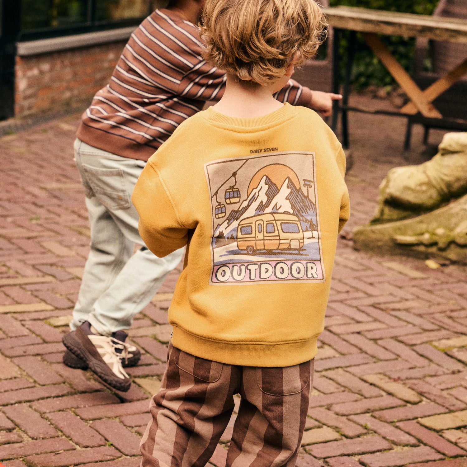 Kind trägt das orangefarbene Daily Seven Sweatshirt im Alltag