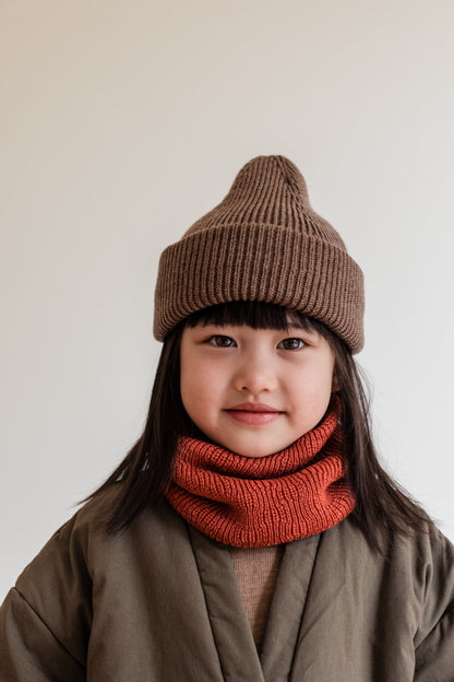 Kind trägt den Hvid Gigi Loop Schal Merino in Wild Berry zur braunen Mütze, erhältlich bei Bärechind