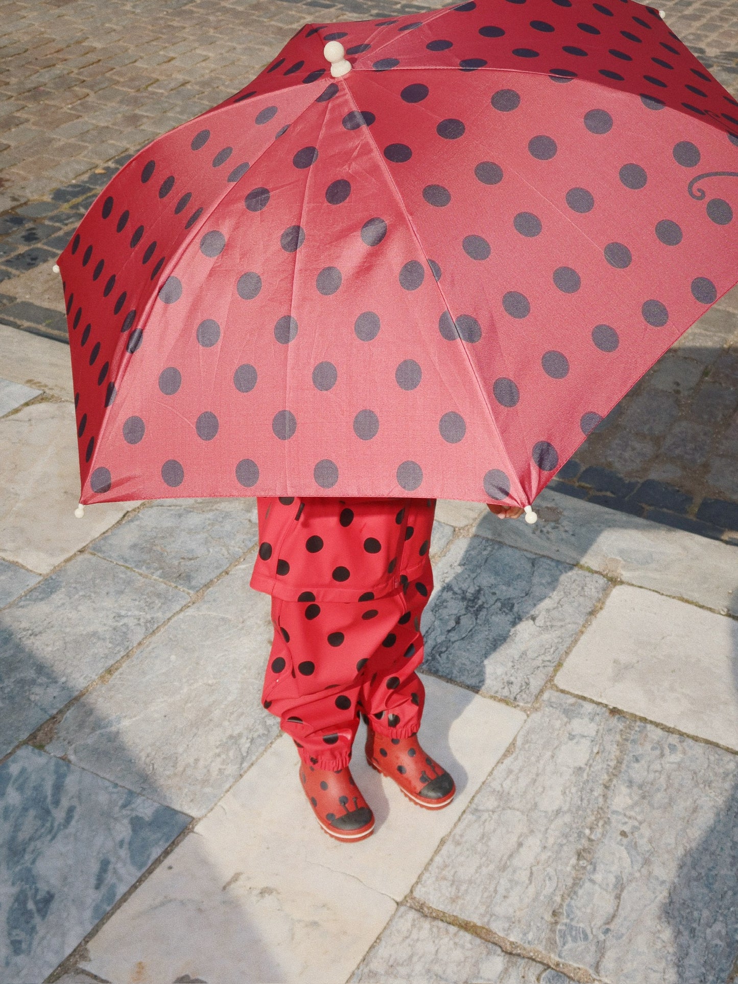 Kind mit geöffnetem Marienkäfer-Regenschirm auf dem Spaziergang