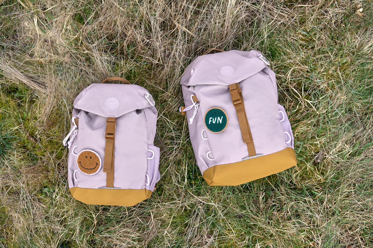 Zwei Lässig Wanderrucksäcke Little Gang in Lilac im Gras, nachhaltige Wahl für kleine Entdecker, im Bärechind Winterthur.