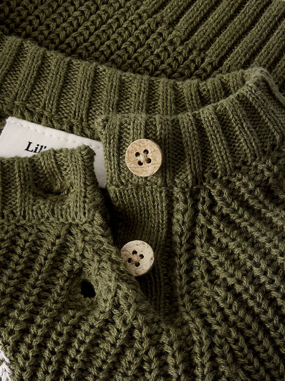 Detailaufnahme der Schulterknöpfe und des groben Strickmusters des Baby Pullovers von Lil' Atelier in Olivgrün.