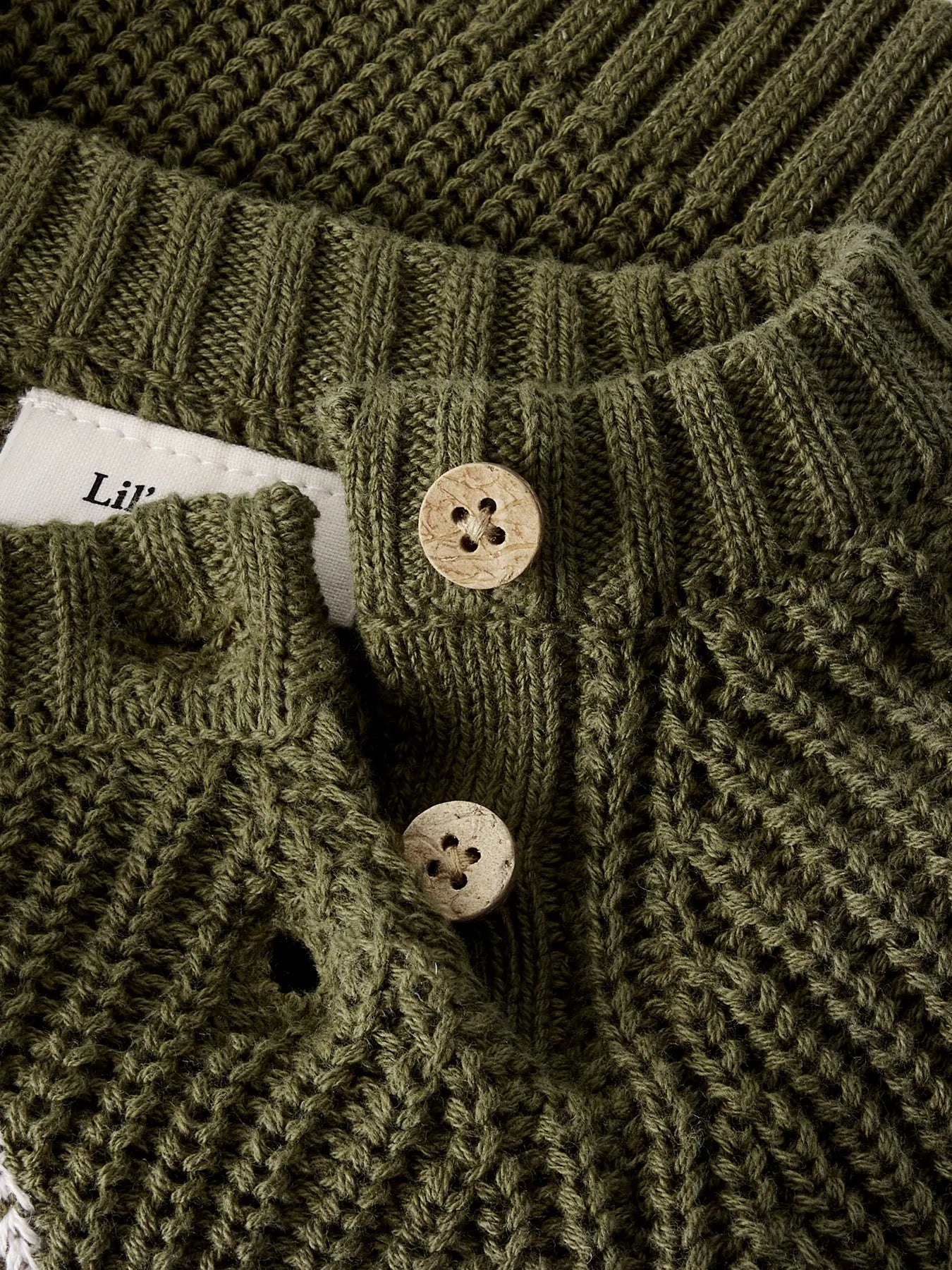 Detailaufnahme der Schulterknöpfe und des groben Strickmusters des Baby Pullovers von Lil' Atelier in Olivgrün.