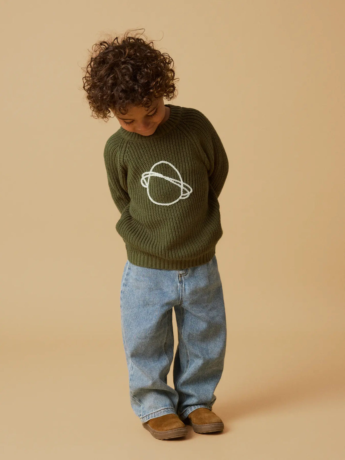 Kind trägt den olivgrünen Strickpullover mit Planetenmotiv von Lil' Atelier kombiniert mit einer Jeans. Erhältlich im Bärechind Winterthur.