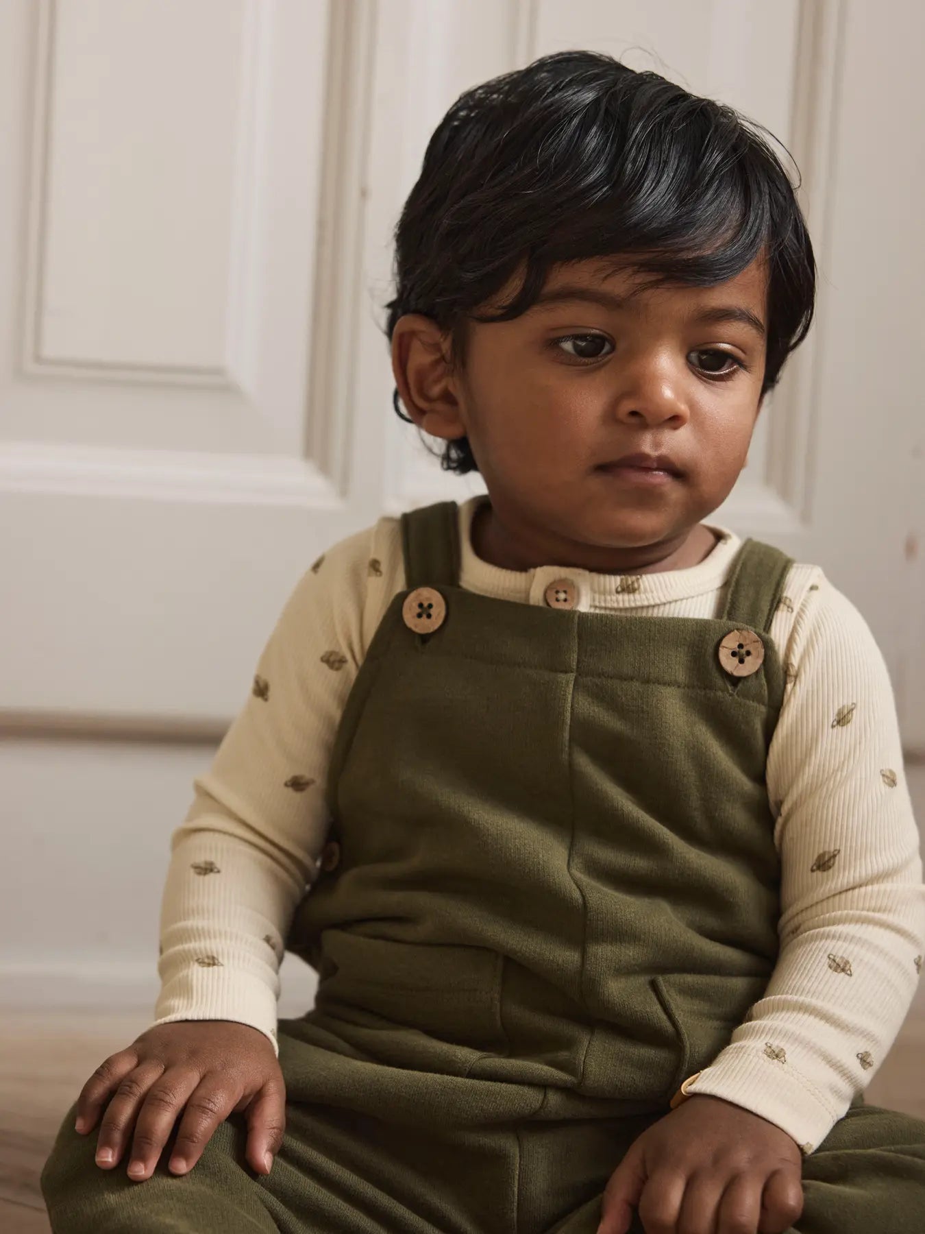 Baby trägt den LIL' ATELIER Ripp Body aus Baumwolle und TENCEL™ Lyocell in Creme mit kleinem Planetenprint