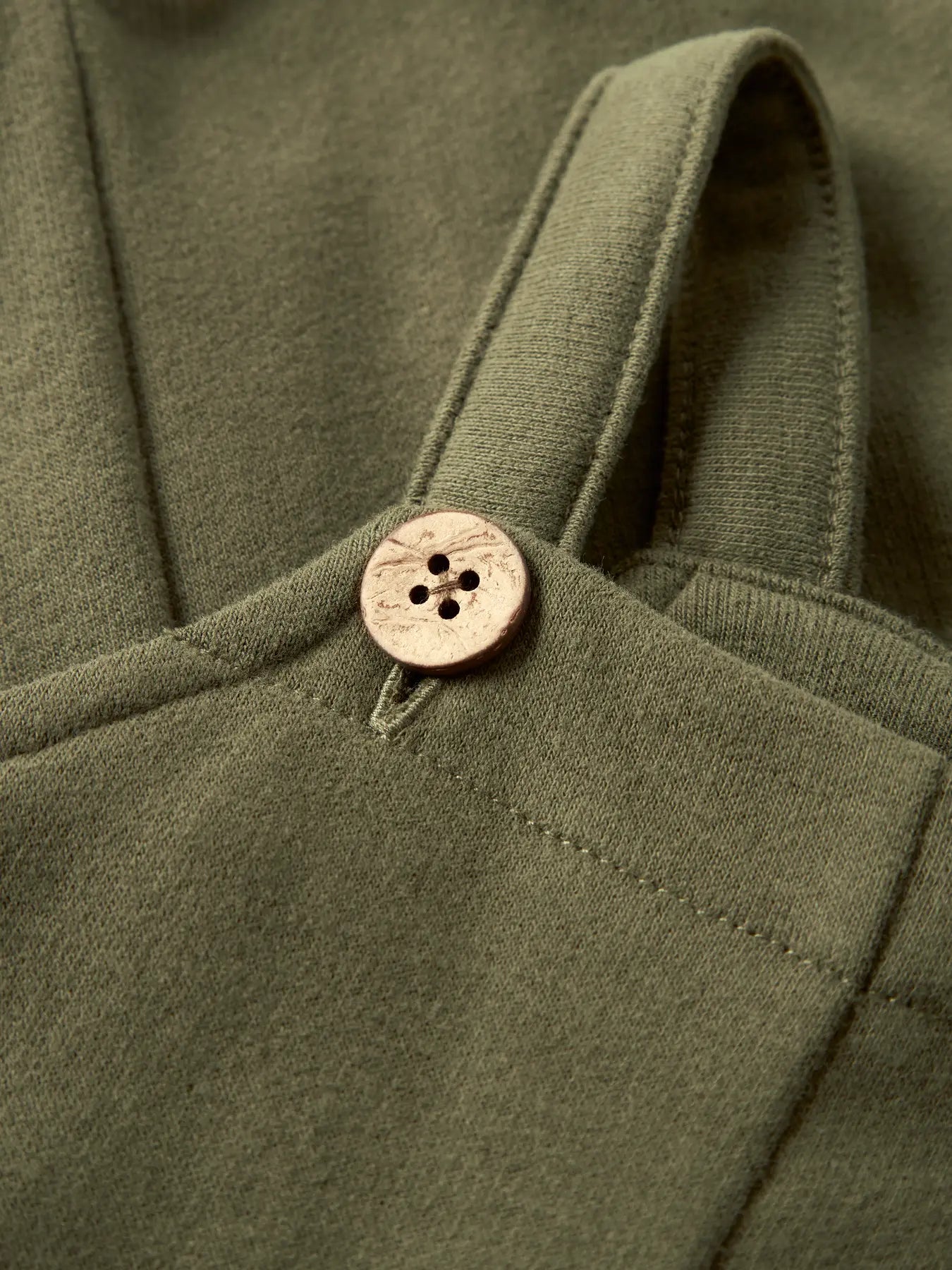 Detailaufnahme der LIL' ATELIER Sweat Latzhose aus Bio Baumwolle in Olivgrün mit Trägern und Knöpfen in Holzoptik
