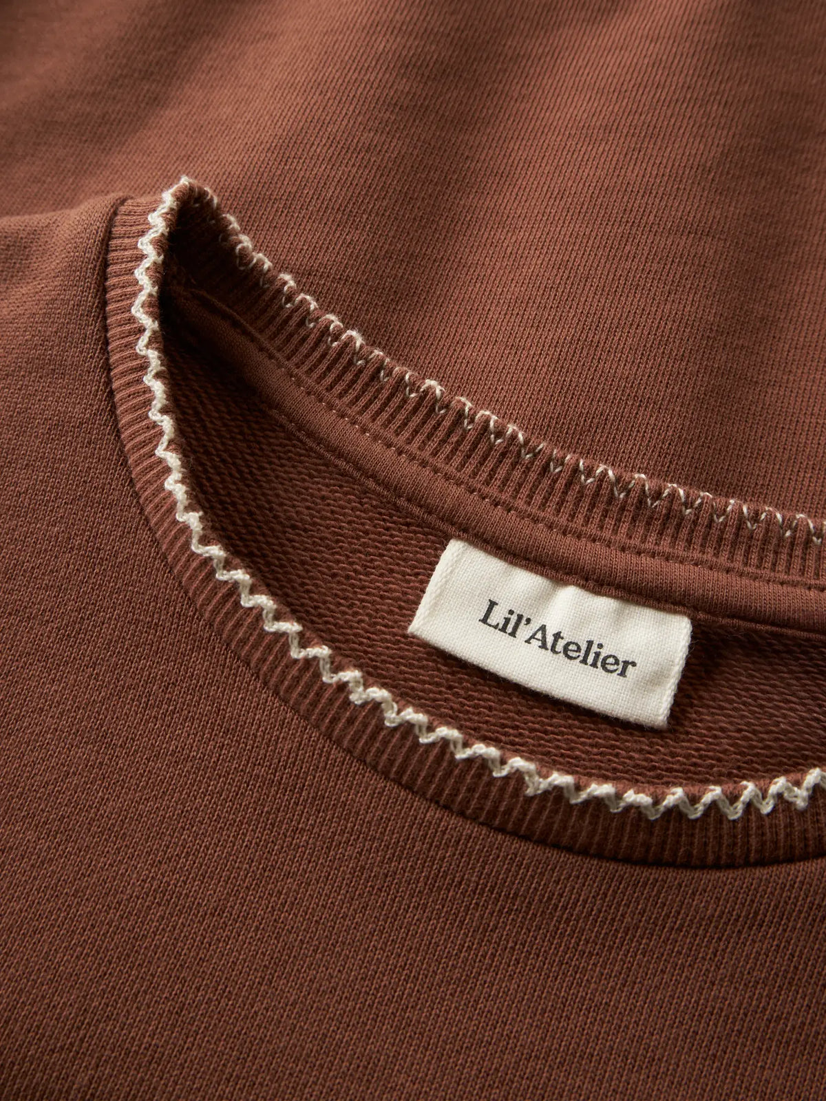 Detailaufnahme des LIL' ATELIER Sweatshirts aus Bio Baumwolle in rostbraun mit kontrastfarbener Ziernaht