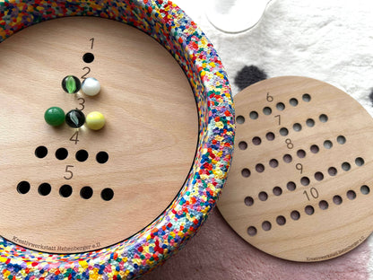 Das Montessori Lernspiel aus Holz mit Zahlenfeld und farbigen Murmeln unterstützt Kinder beim spielerischen Erlernen von Zahlen und Mengen.