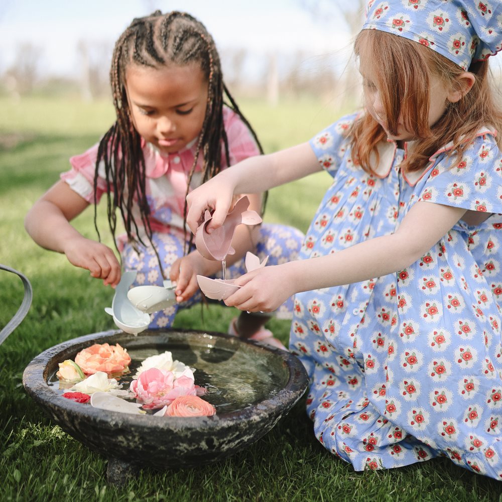 Kinder spielen draussen mit dem Mushie Whale Badespielzeug und entdecken das Schöpfen und Ausgiessen von Wasser.