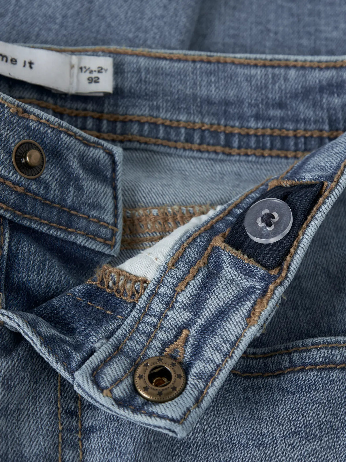 Detailaufnahme der NAME IT Kinderjeans mit Knopf, Gürtelschlaufen und Denimstruktur.