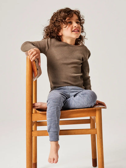 Kind sitzt auf Holzstuhl mit Name it Wollrib Leggings aus Merinowolle in Folkstone