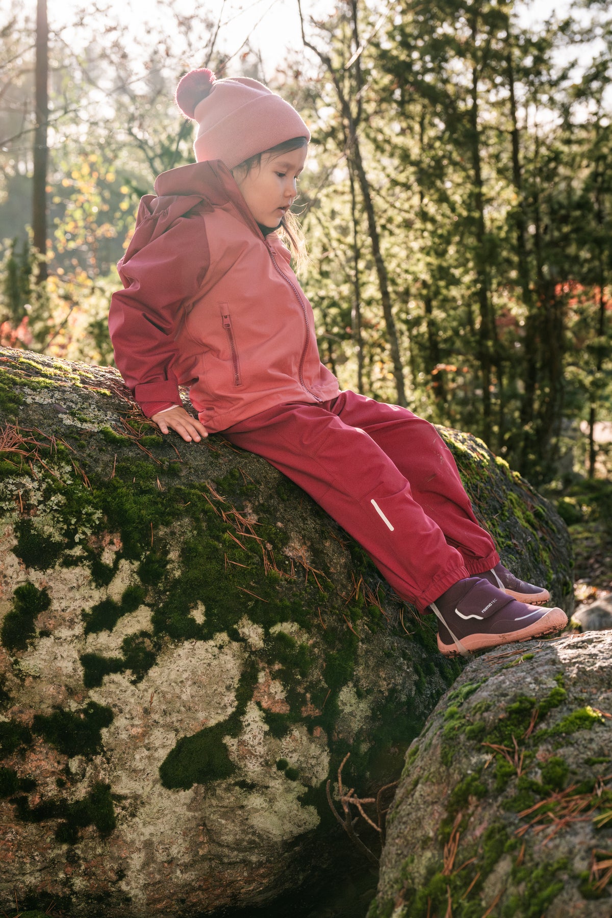 Kind trägt die Reima Kaura Regenhose Cranberry beim Klettern im Wald