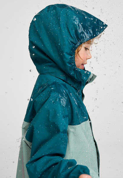 Kind seitlich trägt ReimaTec Regenjacke Salmi in Stone Green bei Regenwetter