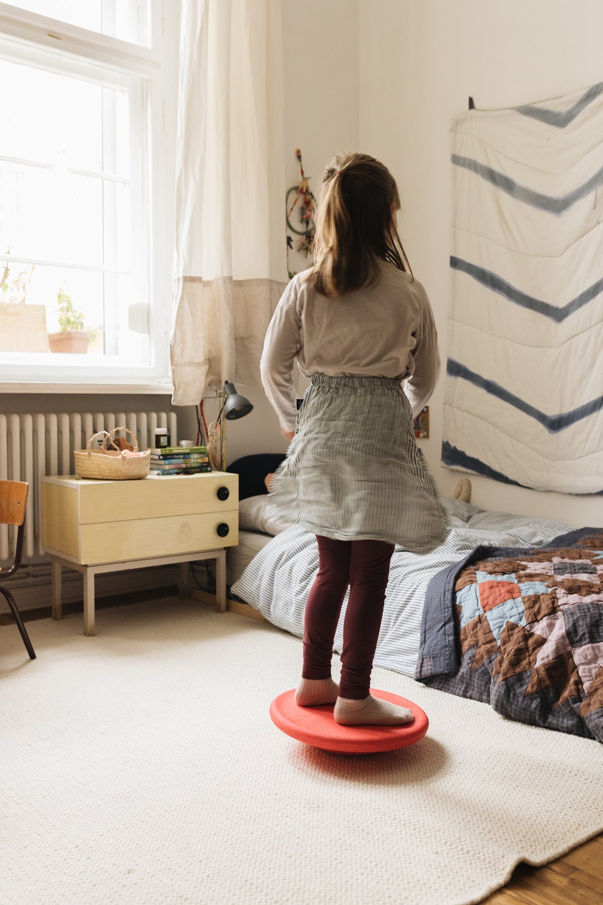 Kind spielt auf rotem Balance Board im Kinderzimmer – Bewegung drinnen mit Stapelstein