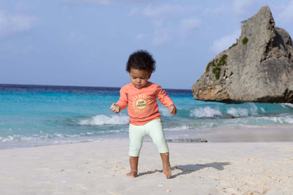 Kind trägt LÄSSIG UV-Shirt in Koralle beim Spielen am Strand – erhältlich bei Bärechind in Winterthur, Zürich, Schweiz.